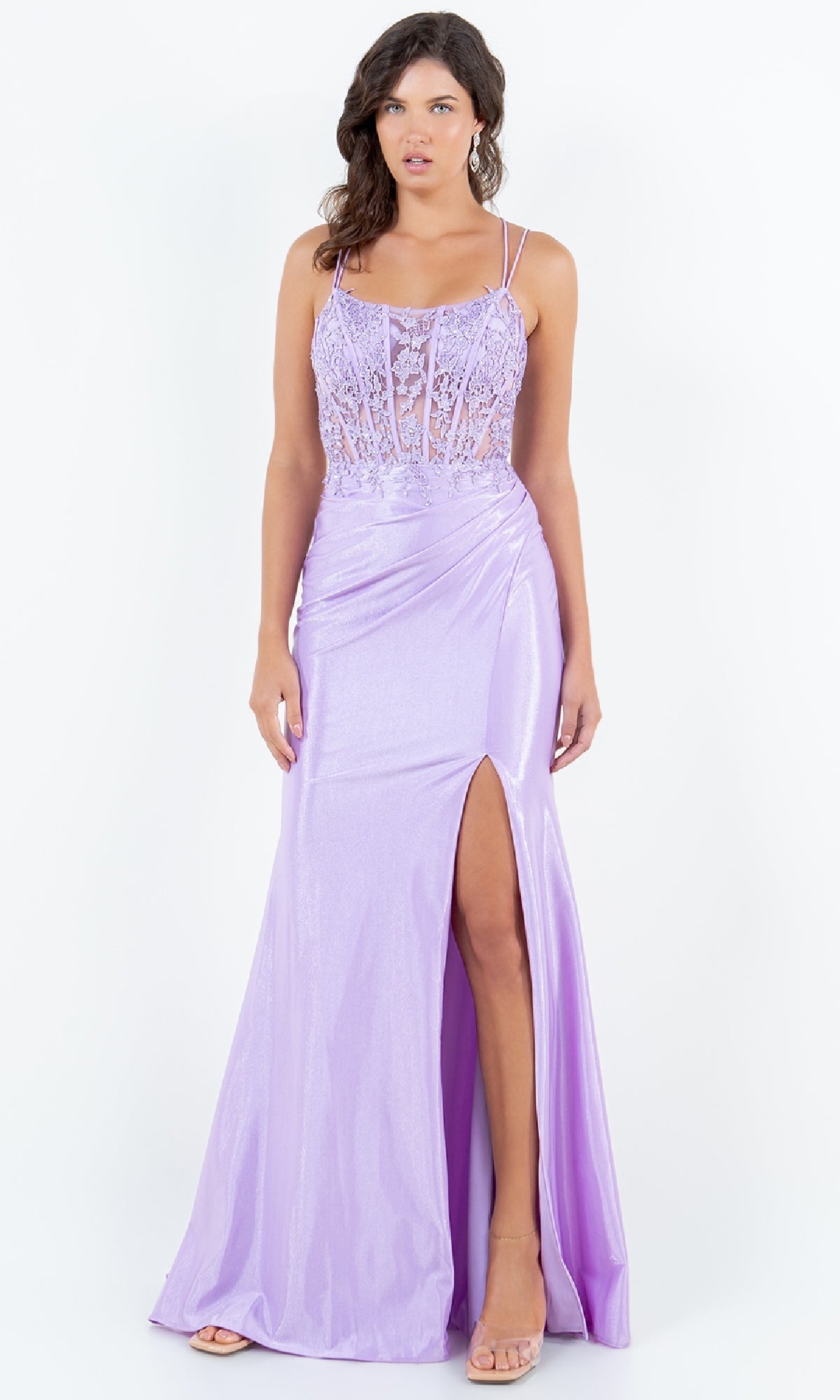 A woman models the Lace-Up Lilac Prom Gown (Cinderella Couture 8185J), featuring thin straps, a lace bodice, and a thigh-high slit, standing against a white background.